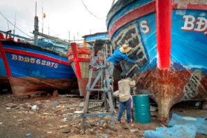 A group of men working together to repair fishing boats in a shipyard setting.